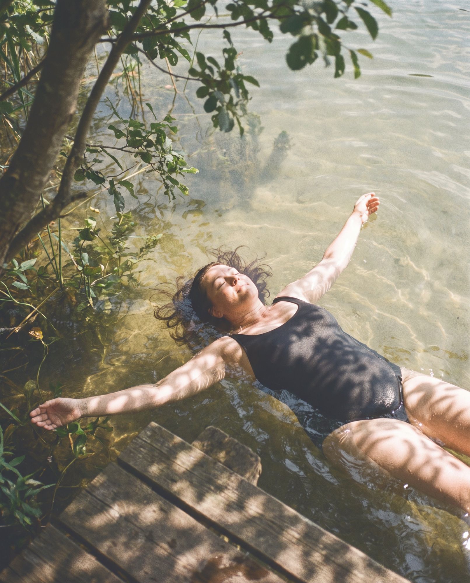 A woman floating on her back in a clear lake, arms open.