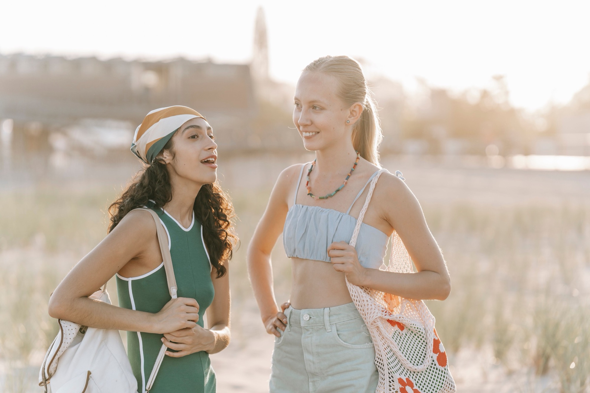 Two friends talking on the dunes at golden hour, one speaking, the other smiling as she listens.