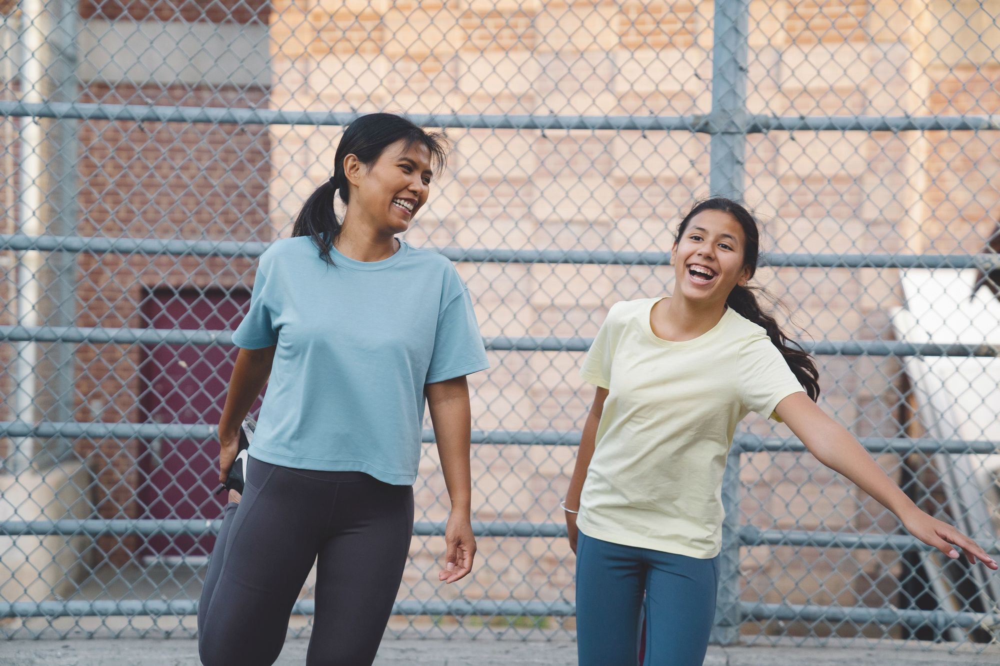 Two women laughing together outdoors, in powder blue and pale yellow.