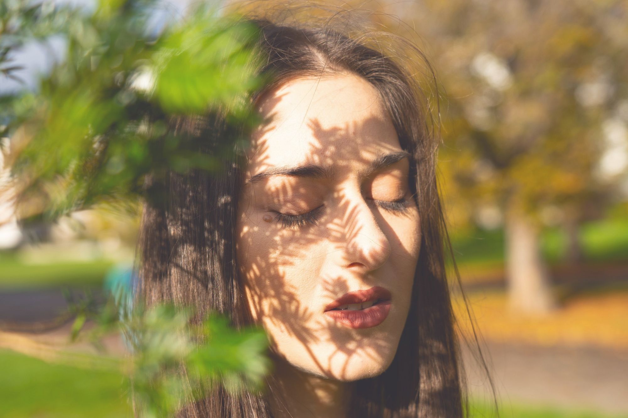 A woman with her eyes closed, leaf shadows across her face.